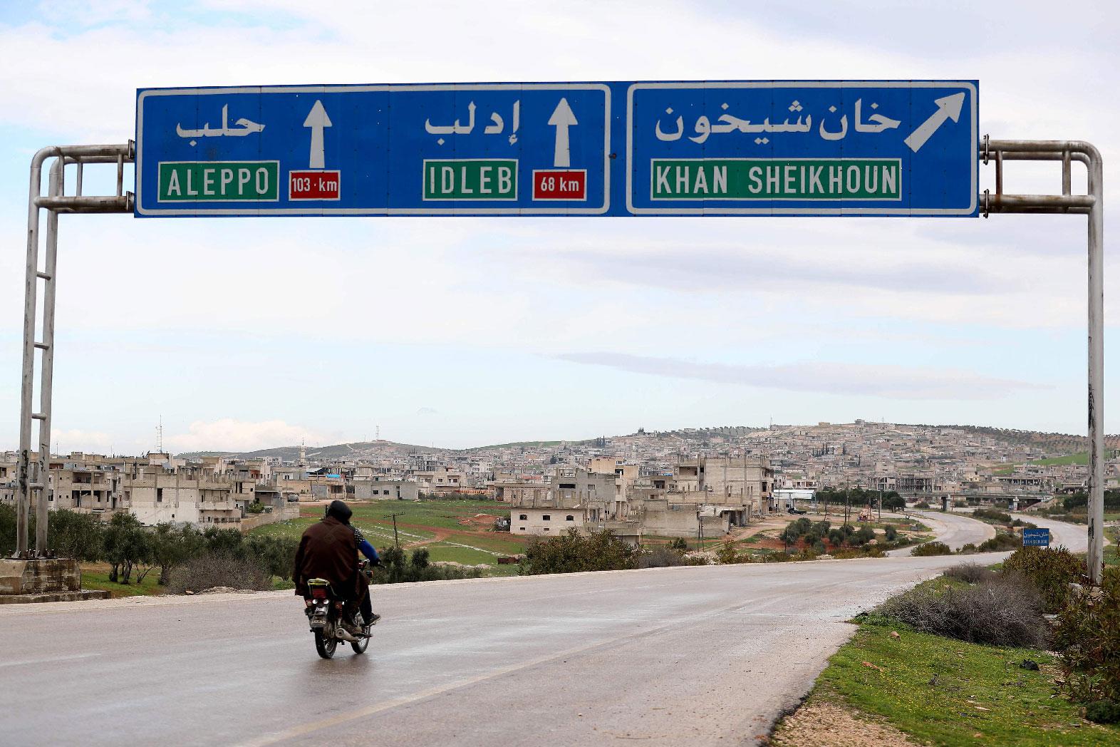 Two Syrian men drive past road signs in Khan Sheikhun on February 28, 2019.