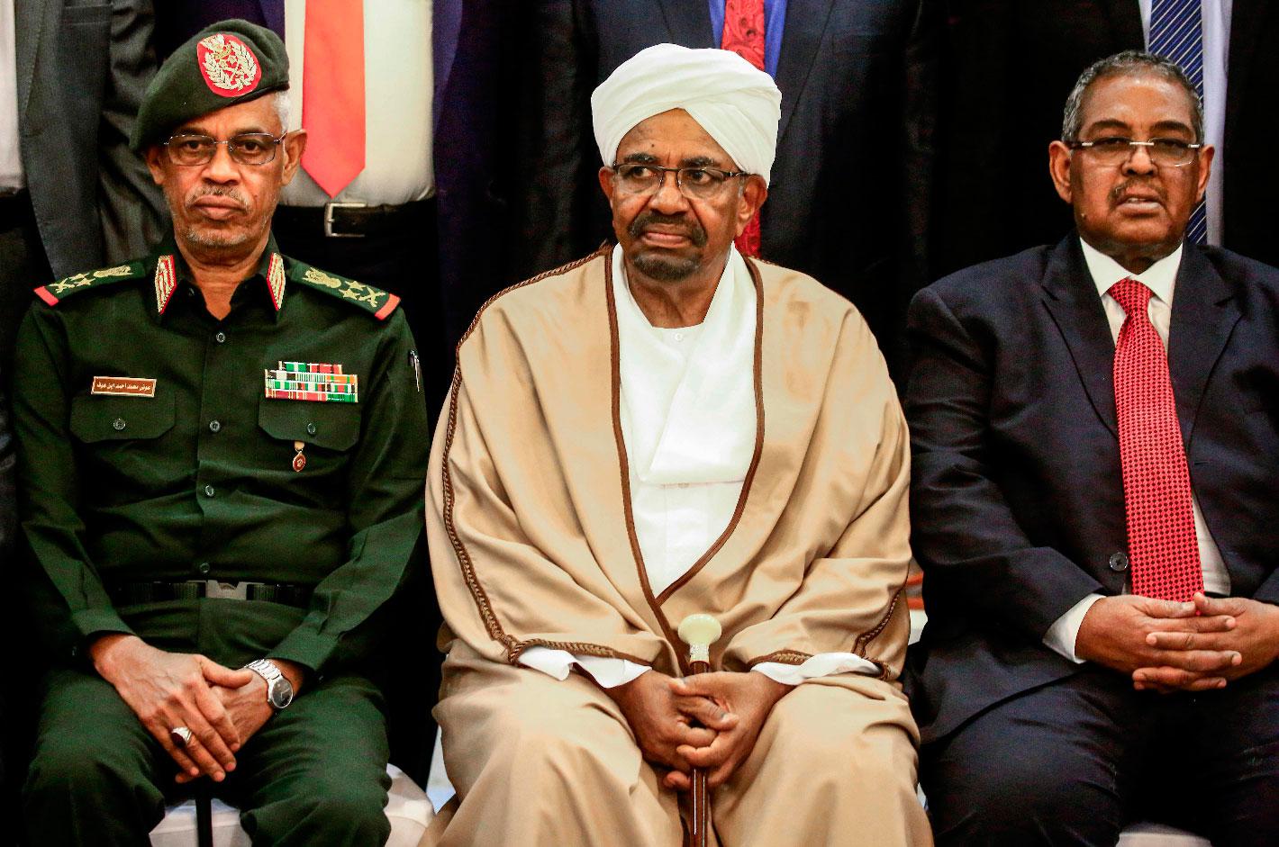 Sudan's President Omar al-Bashir (C) is seated alongside his first vice president Lieutenant General Awad Mohamed Ahmed ibn Auf (L) and Prime Minister Mohamed Tahir Eila (R) as they pose for a group photo with members of the new 20-member cabinet taking oath at the presidential palace in the capital on March 14, 2019.