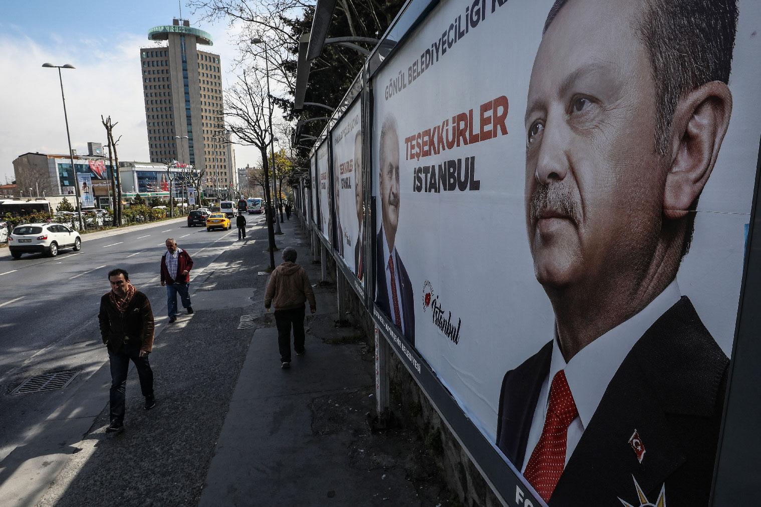 People walk past posters showing Turkey's President Recep Tayyip Erdogan and Binali Yildirim, the mayoral candidate for Istanbul of the ruling Justice and Development Party (AKP) a day after the local elections in Istanbul, Monday, April 1, 2019.