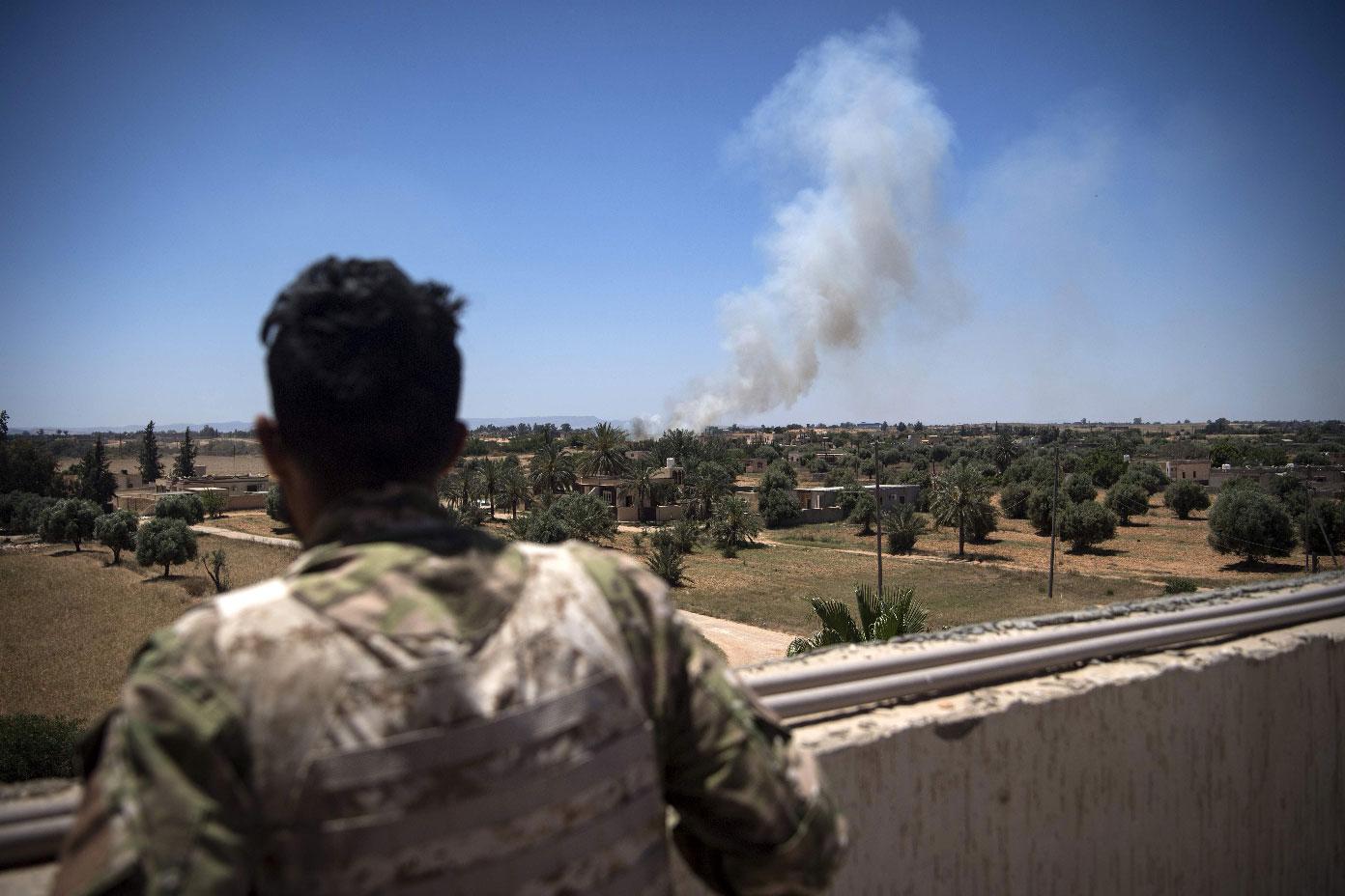 A fighter loyal to the GNA watches as smoke rises in the distance
