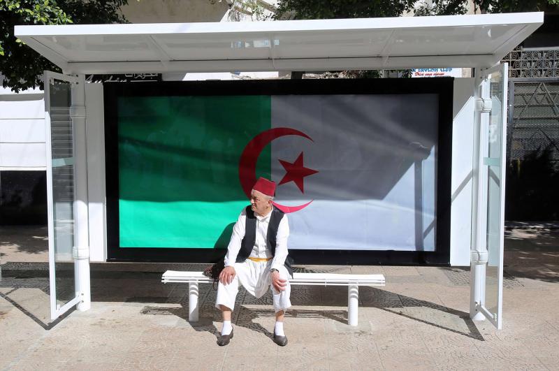 A man sits at a bus station decorated with the national flag in Algiers