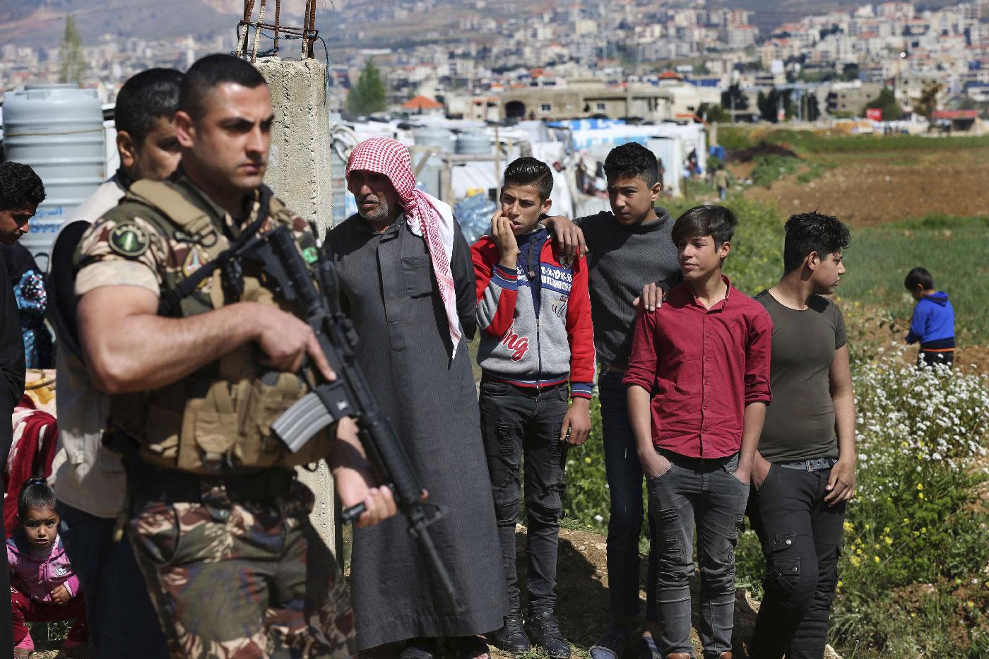 A Lebanese army soldier stand guards in front of Syrian refugees who stand outside their tent to watch the opening ceremony of a school for Syrian refugees, in the Bekaa valley