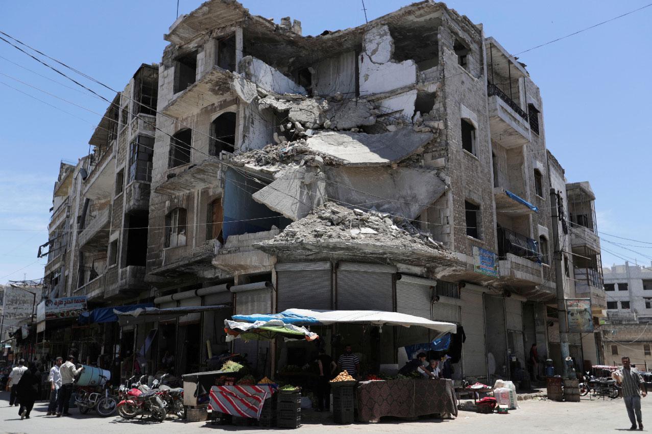 People walk past a damaged building in the city of Idlib