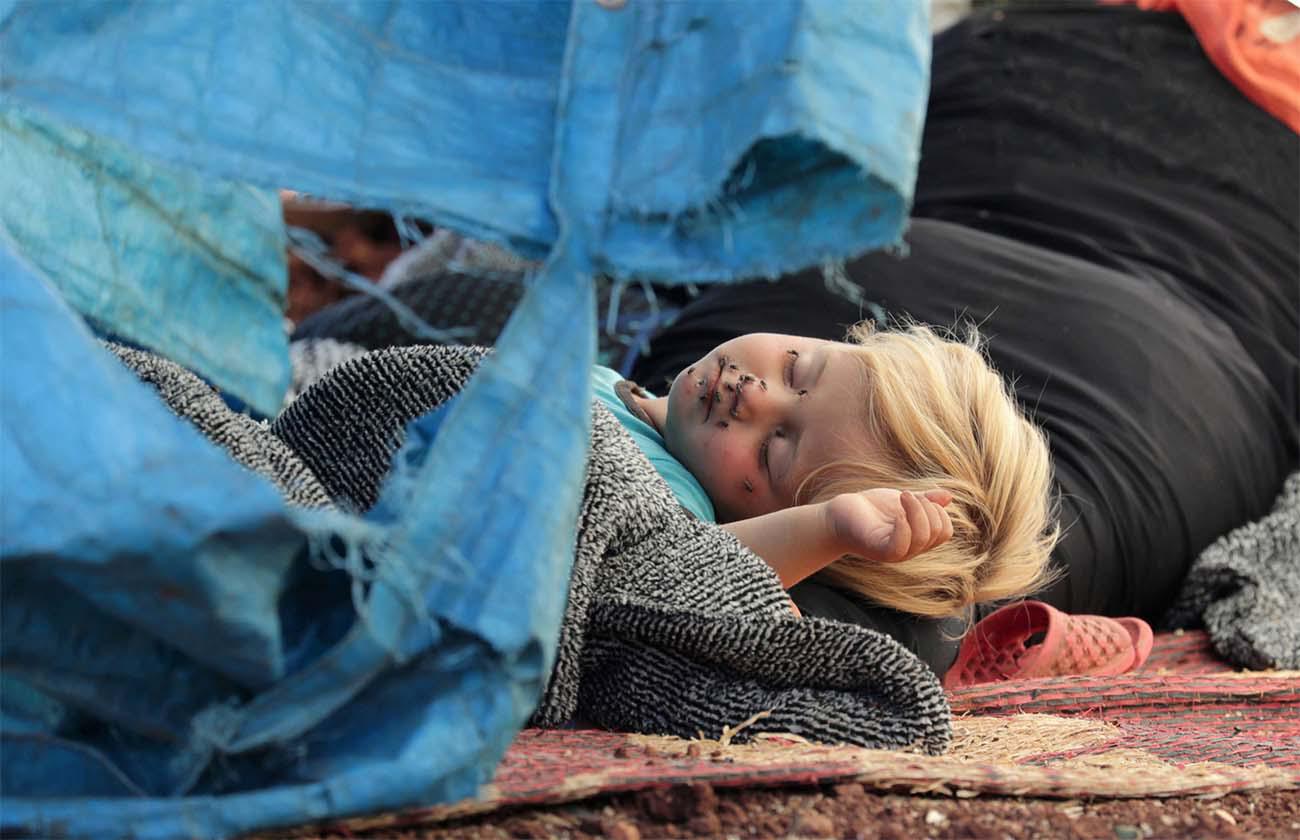 A displaced Syrian child sleeps on a mat laid out on the floor in an olive grove in the town of Atmeh, Syria