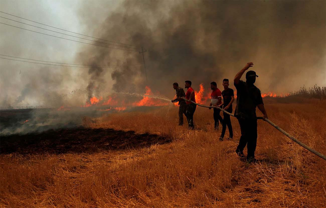 Iraqi farmers and other residents attempt to put out a fire that engulfed a wheat field in the northern town of Bashiqa