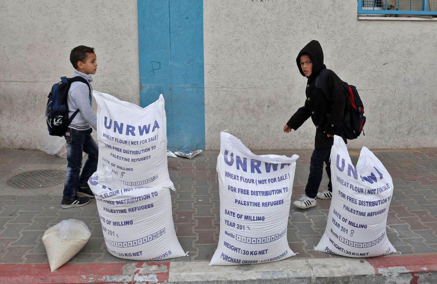 أطفال فلسطينيون يمرون بالقرب من أكياس لوكالة الغوث الدولية في مخيم للاجئين في رفح