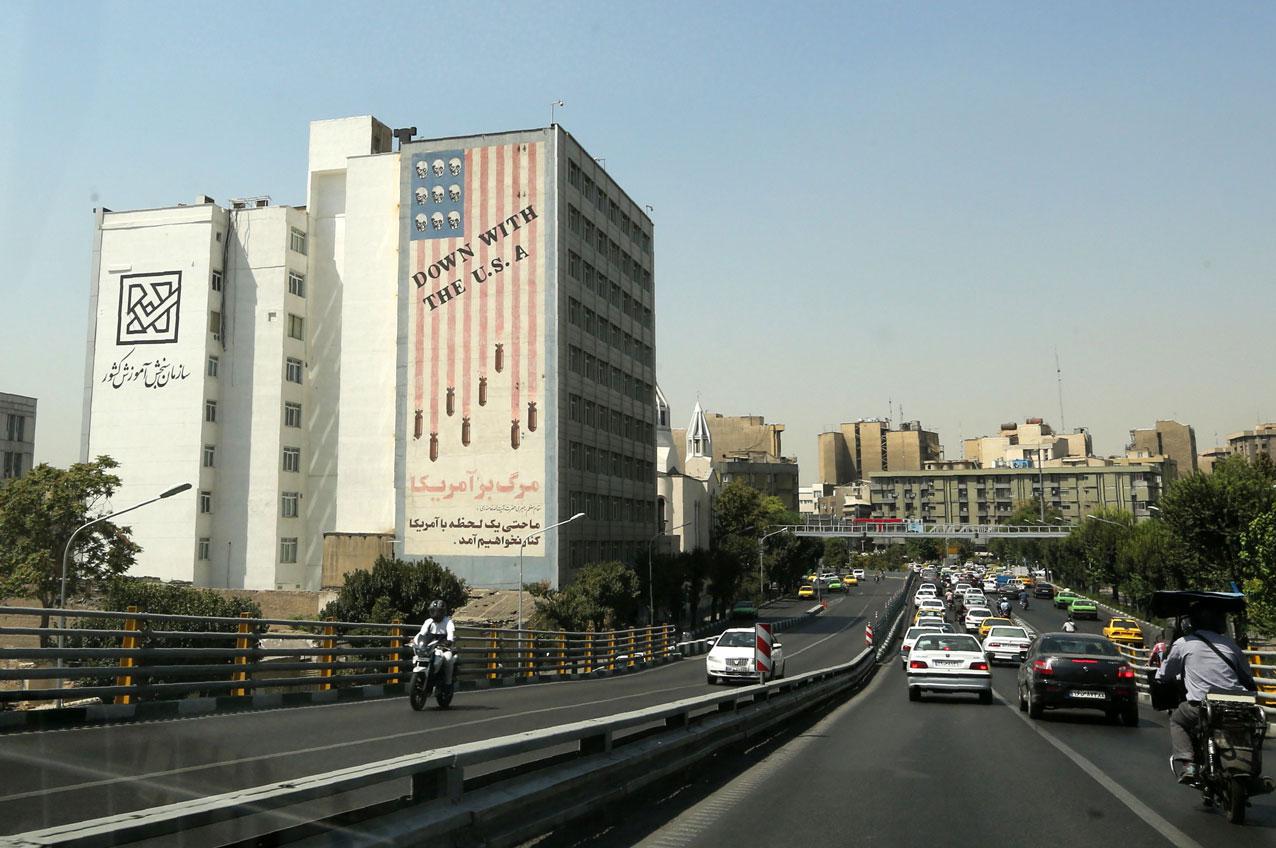 Cars drive past a mural painted on the wall of a building showing an anti US slogan in the capital Tehran