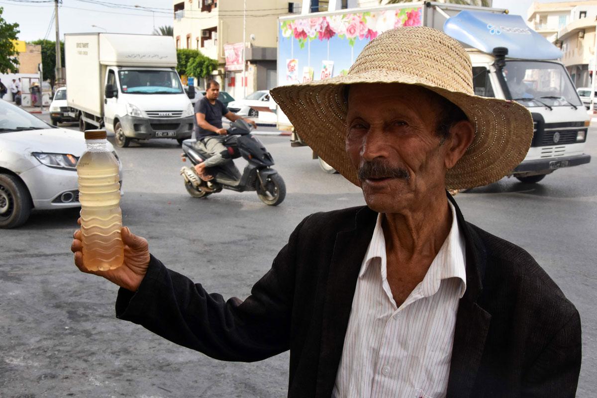 A street vendor holds a bottle of legmi, a coveted date palm drink, in the southwestern Tunisian town of Gabes
