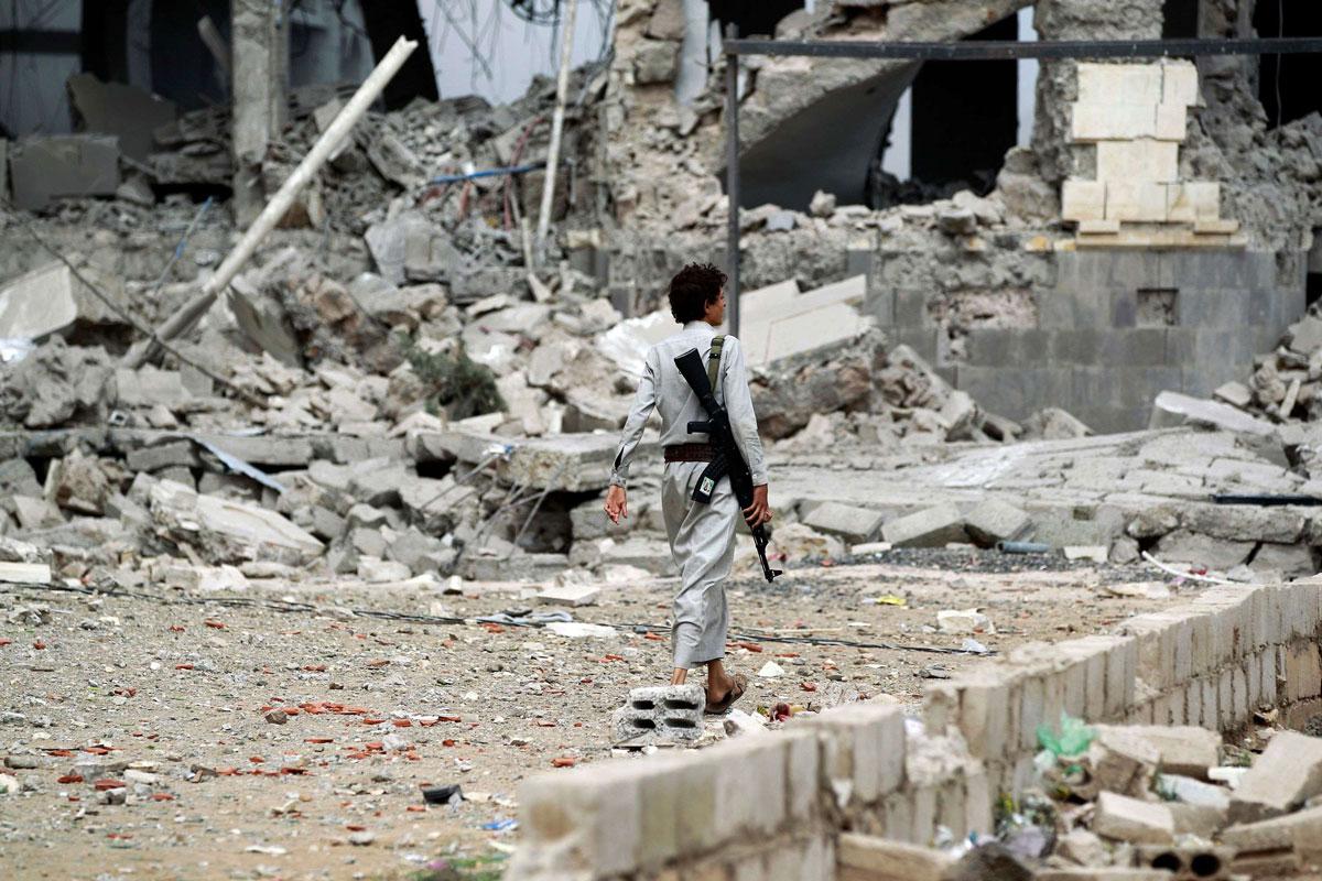 Huthi militant walks amidst the debris of a house