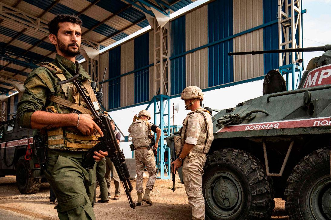 A member (L) of the Syrian Kurdish Asayish internal security forces walks past Russian military police members