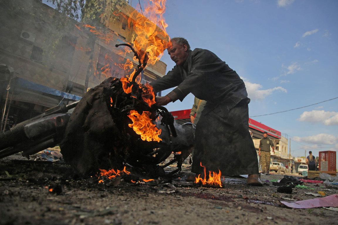 A Syrian man stands next to a burning motorcycle at the site of a car bomb explosion in the northern Syrian Kurdish town of Tel Abyad