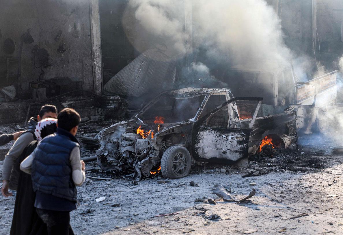 A woman is assisted as she walks past a burning car in Tal Abyad