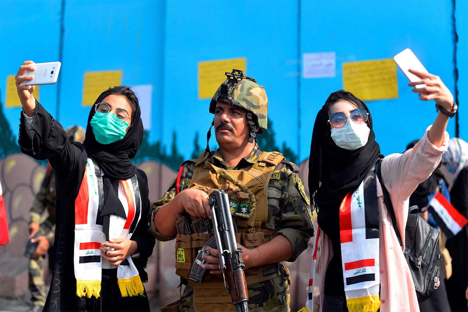 Iraqi students pose for selfies with a member of the security forces during ongoing anti-government protests in Diwaniyah