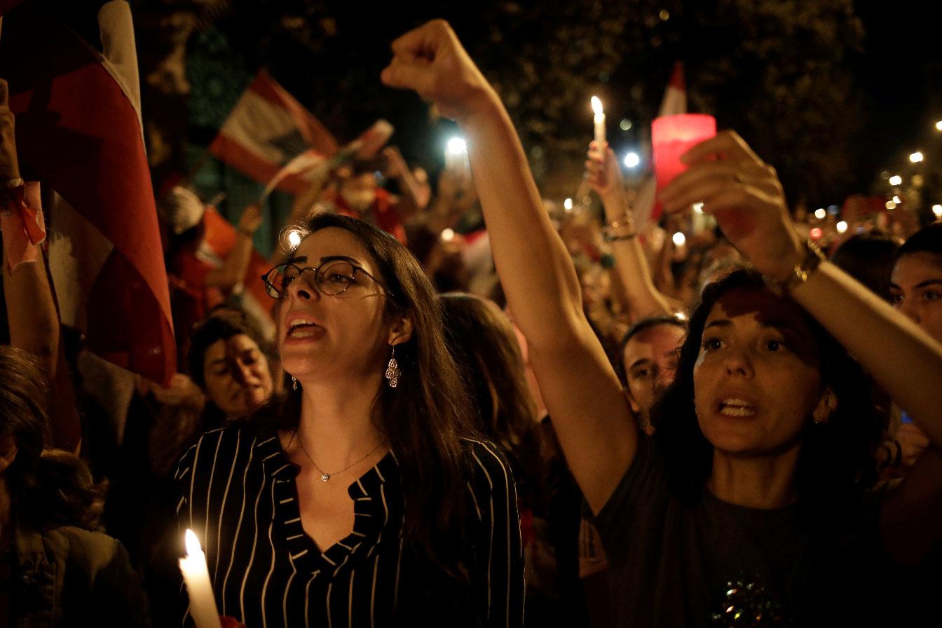 Women gesture and carry candles as they march during ongoing anti-government protests in Beirut