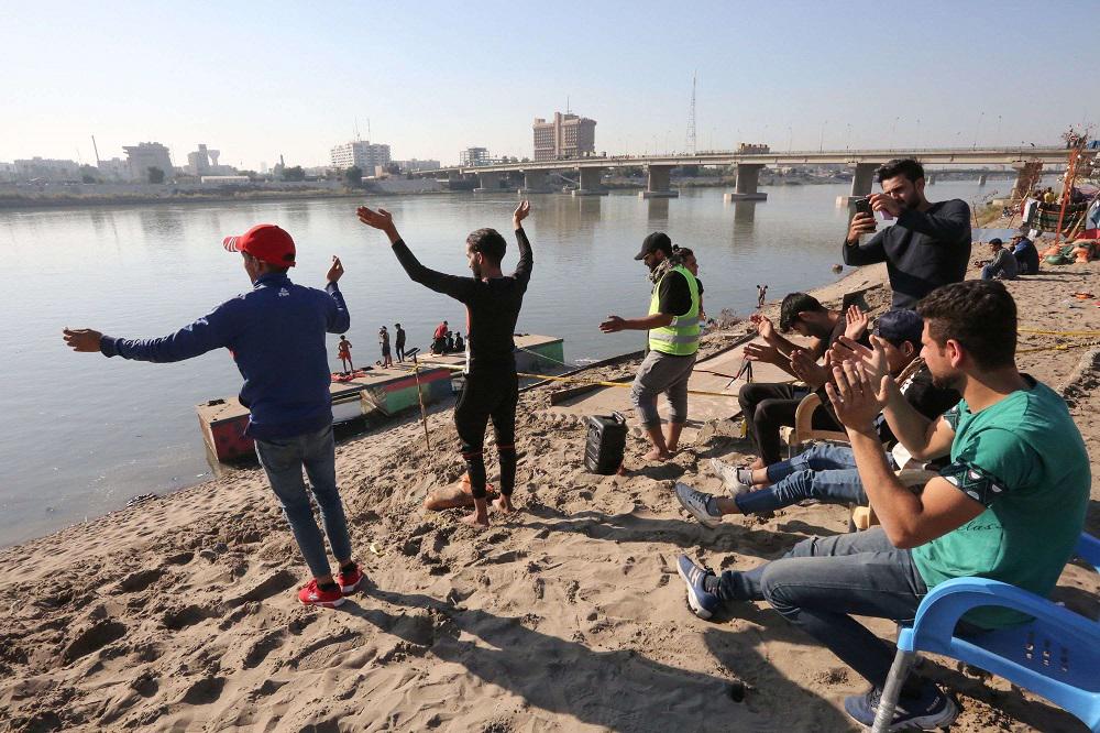 عراقيون يرقصون ويلوحون وهم يبحرون على ضفة نهر دجلة في العاصمة بغداد