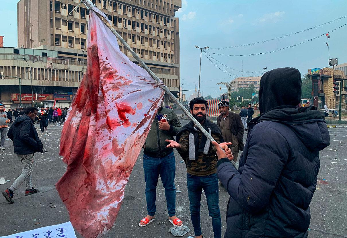 A protester holds a blood-stained flag at the site of an attack by gunmen in Baghdad