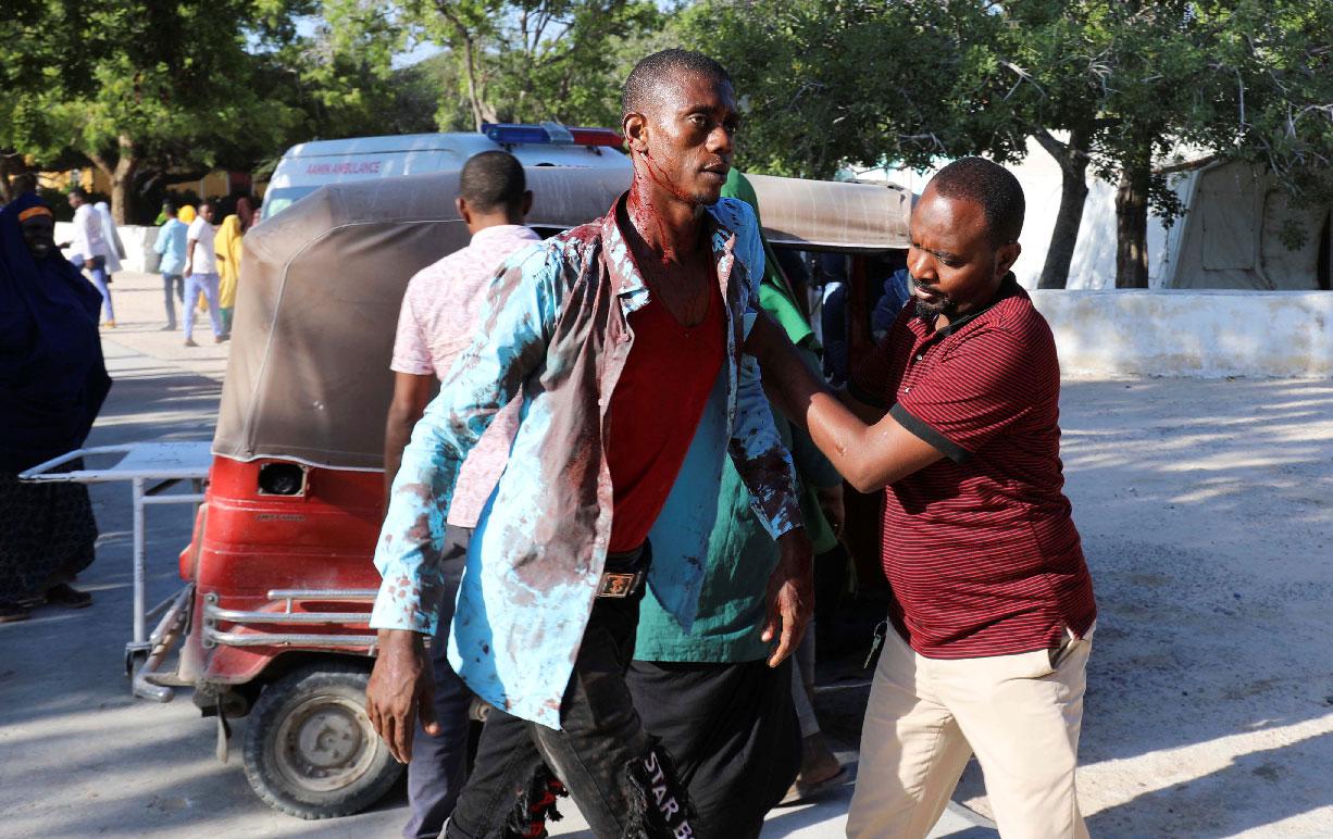 A man assists a civilian injured at the scene of a car bomb explosion at a checkpoint in Mogadishu