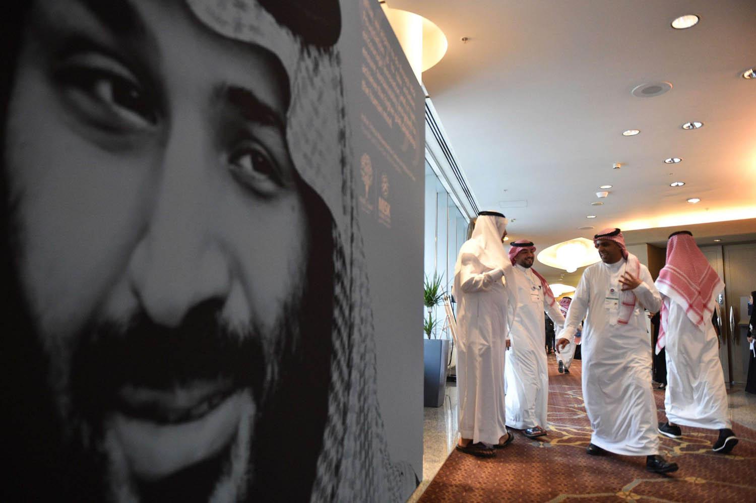 سعوديون يمرون بجانب صورة كبيرة لولي العهد الأمير محمد بن سلمان