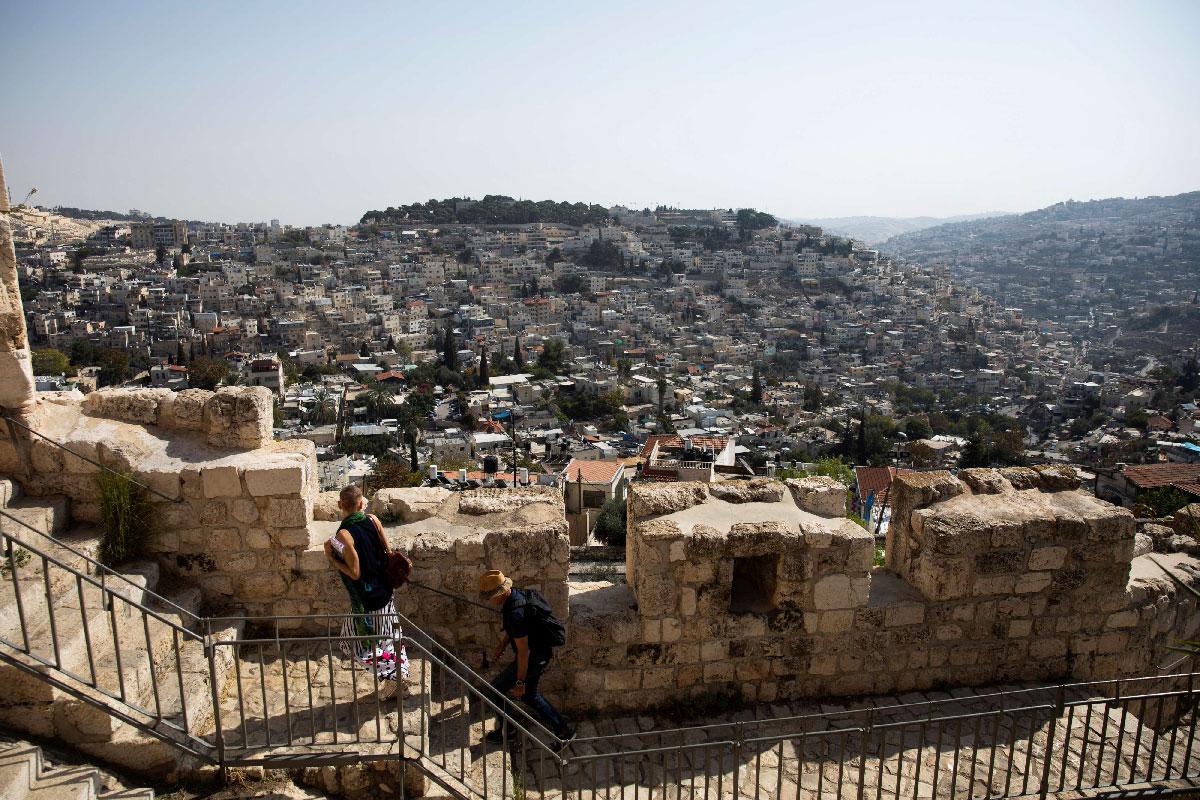 The Palestinian neighborhood of Silwan is seen in the background as people walk on a promenade on the surrounding walls of Jerusalem's Old City