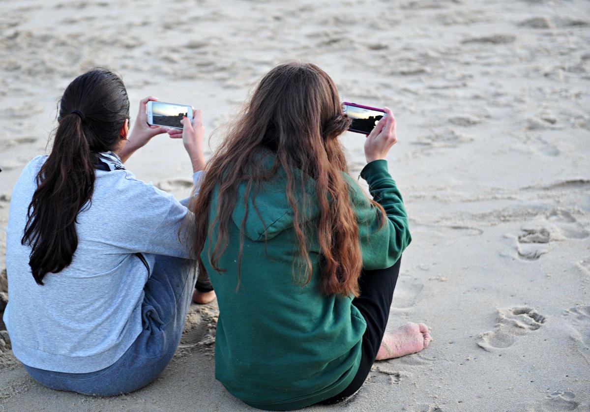 فتاتان تستخدمان هاتفيهما على أحد الشواطئ