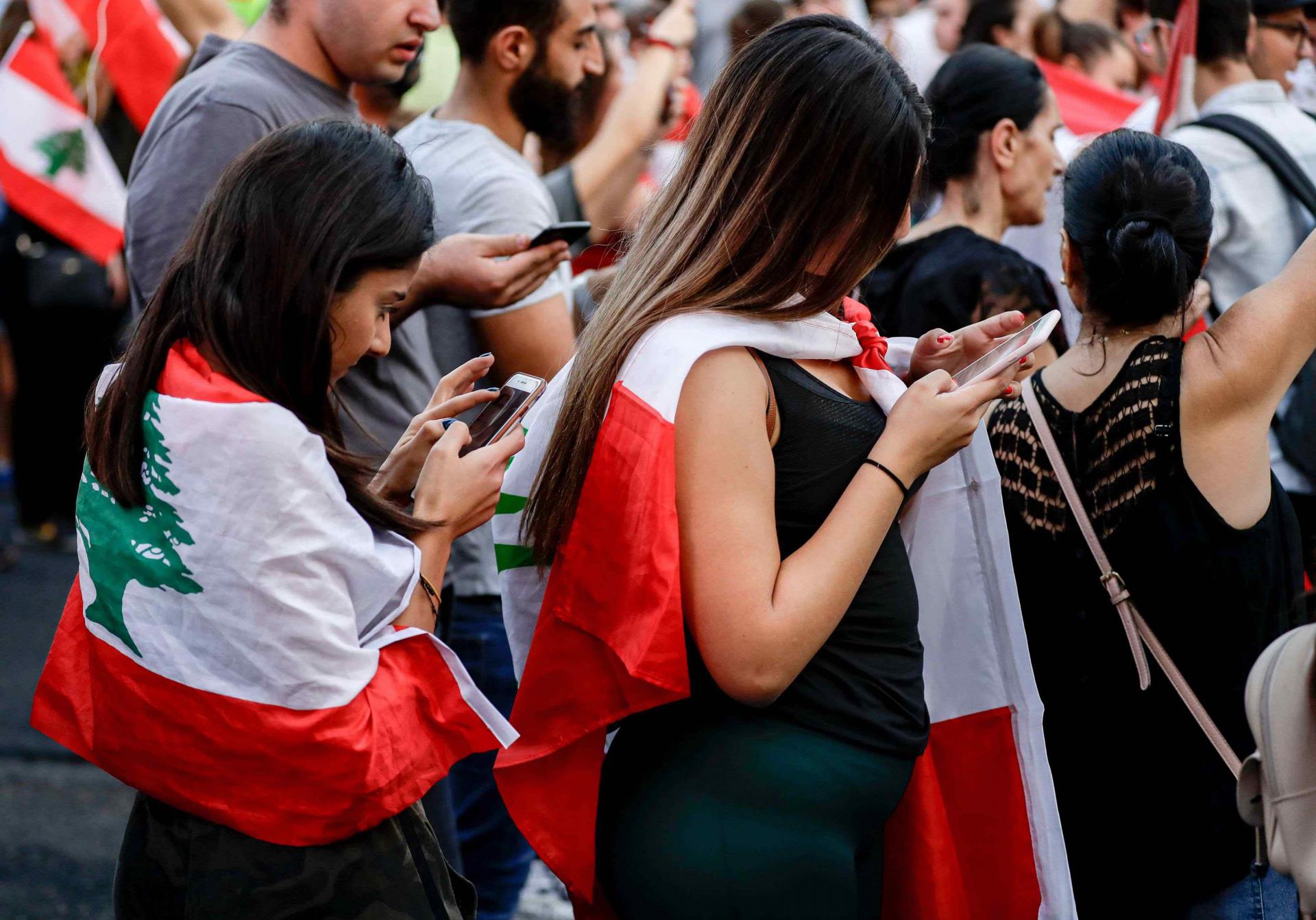 Women draped in the Lebanese national flag use their cell phones during a demonstration against tax increases and official corruption