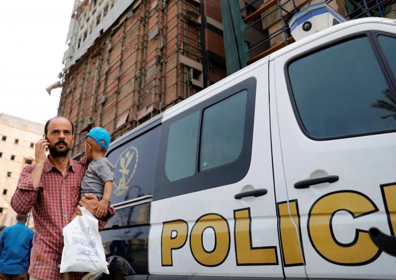An Egyptian man carries his son as he walks past a police car in Cairo.