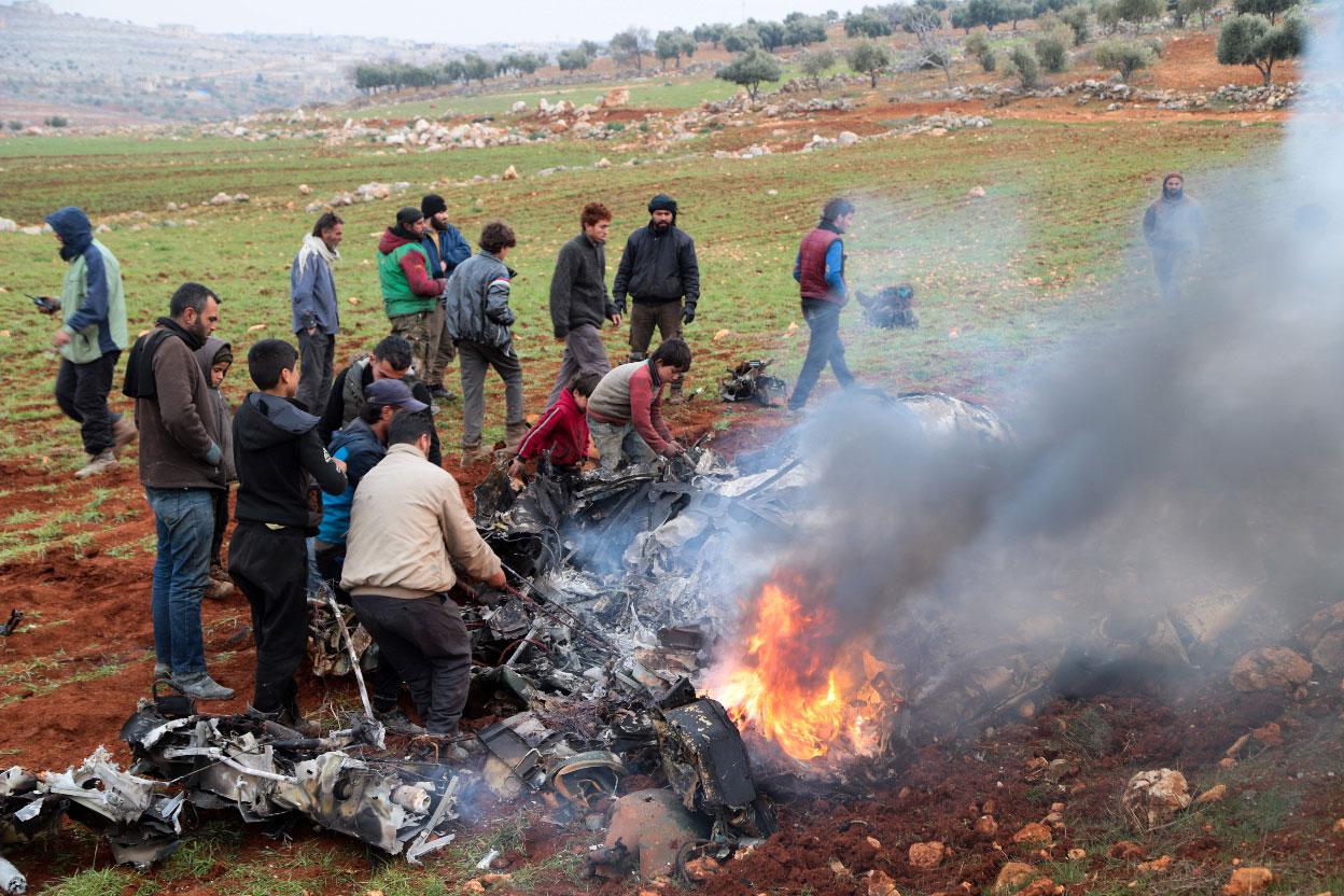 People inspect the wreckage of a military helicopter of the Syrian government forces that was downed over the western Aleppo Province