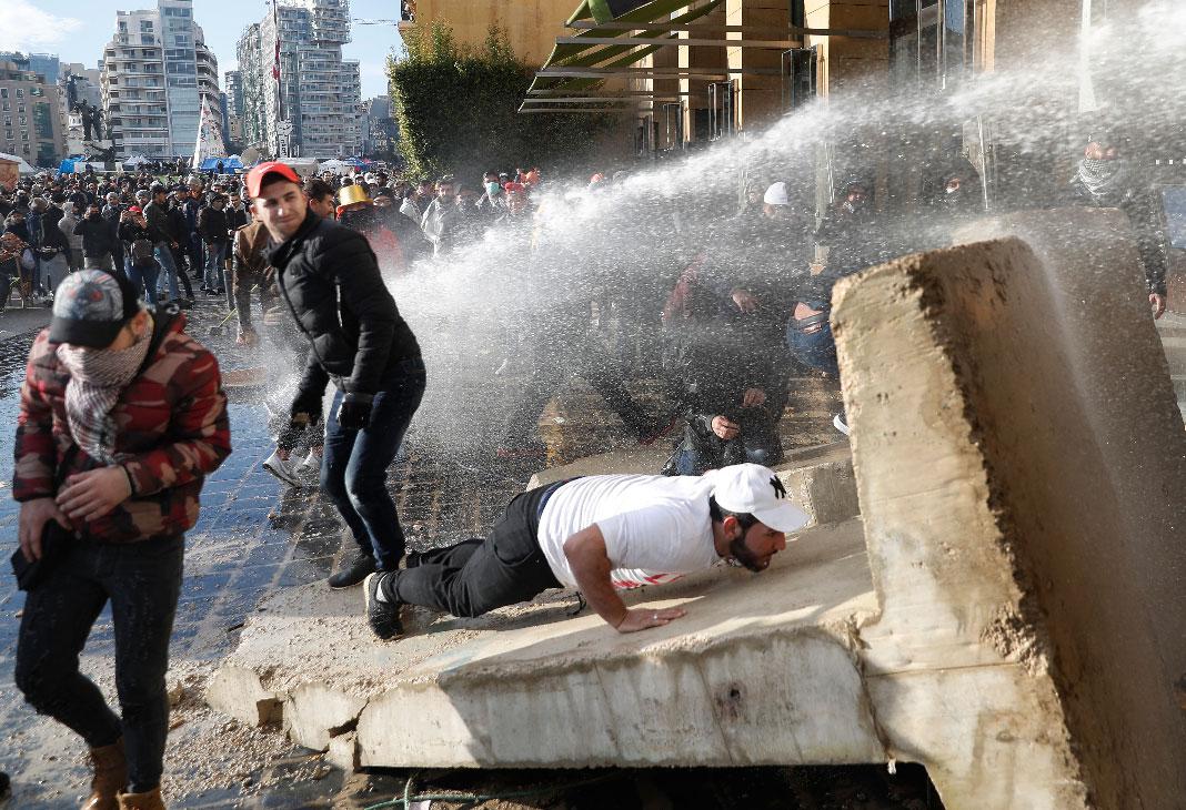 Anti-government protesters are sprayed with a water cannon during a protest, in downtown Beirut