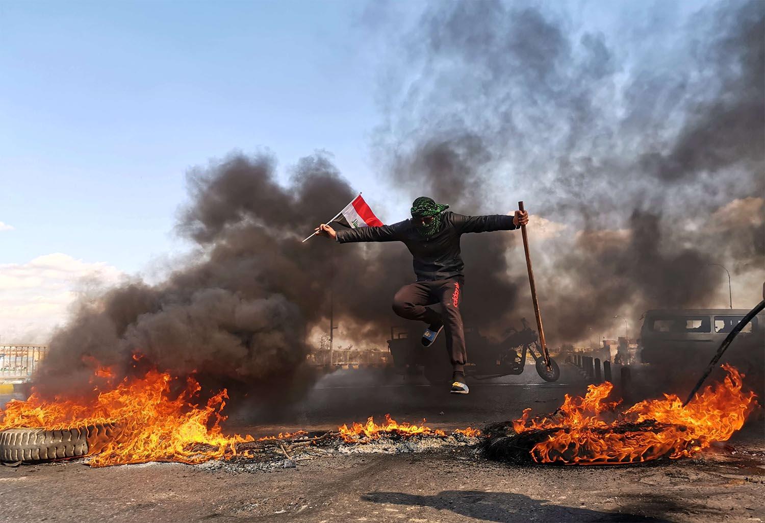 An anti-government protester jumps over burning tires blocking a street during an anti-government protest