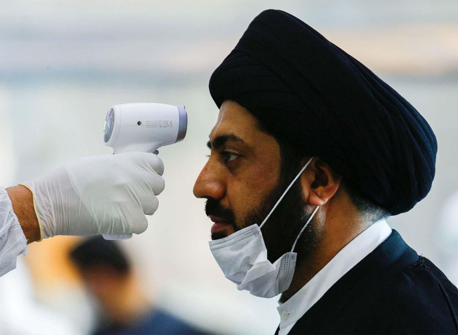 A medical staff member in protective gear checks the temperature of a cleric man amid concerns over the coronavirus (COVID-19) spread at Najaf airport