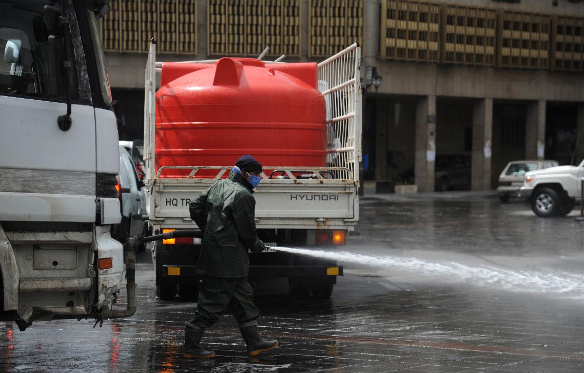 A Syrian worker wearing a protective face mask cleans a street