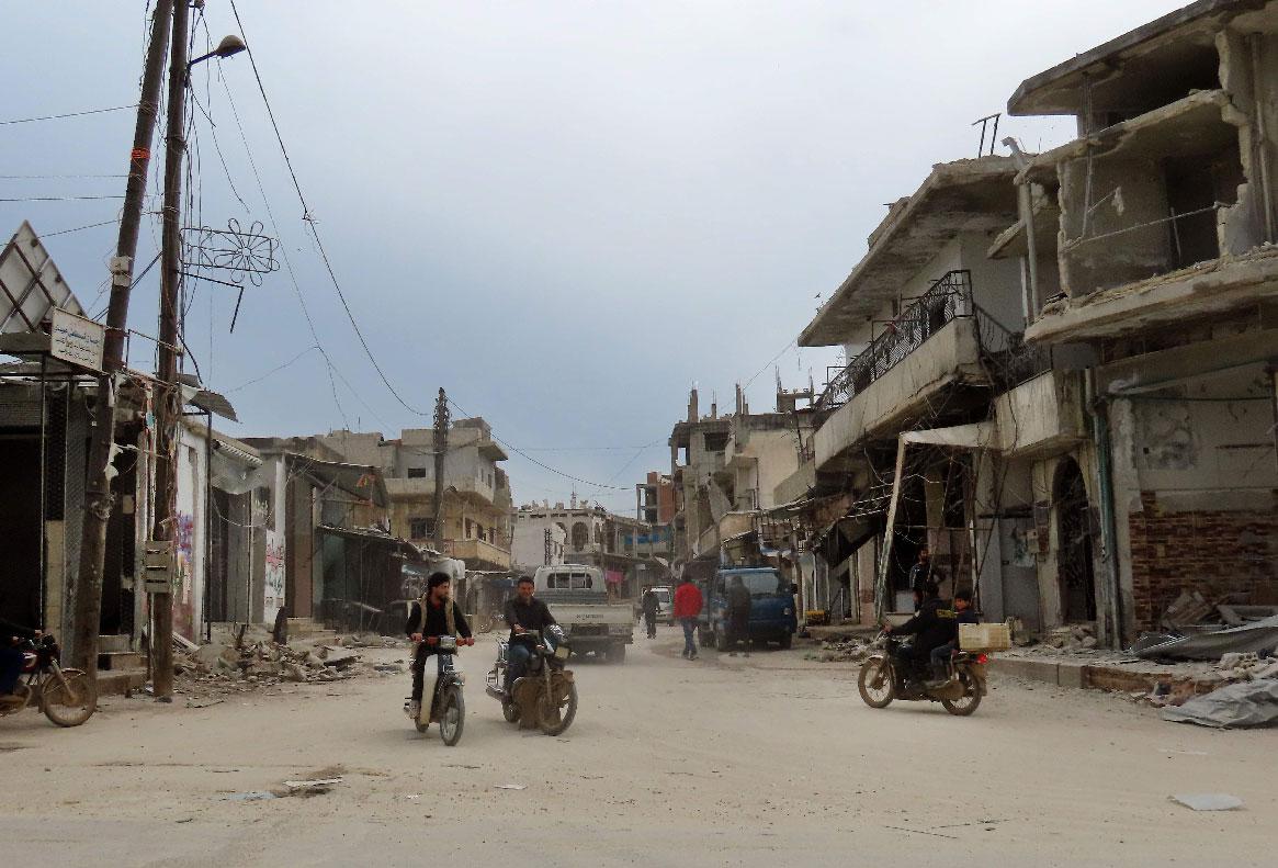 Syrian men ride their motorcycles through a damaged neighbourhood in the town of Binnish