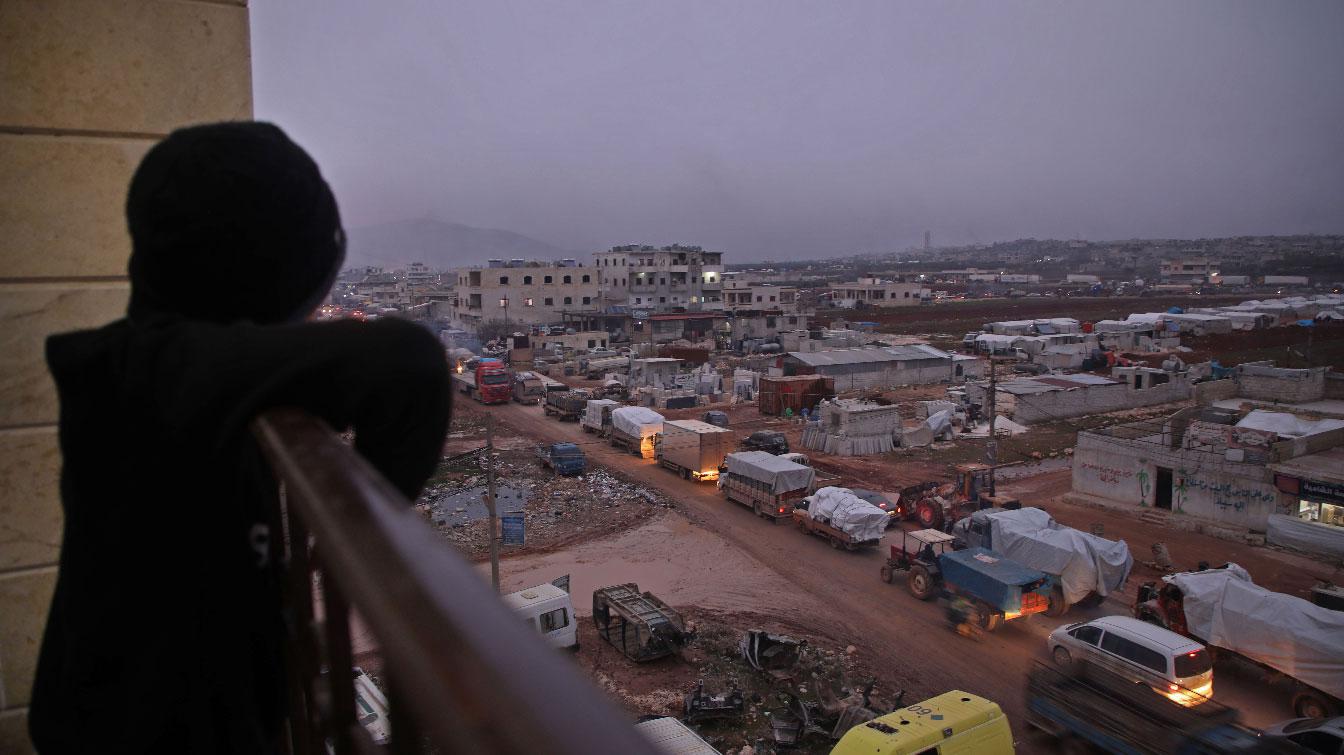 A child in the Syrian town of Dana, Idlib province, watches a large convoy of displaced people from a balcony