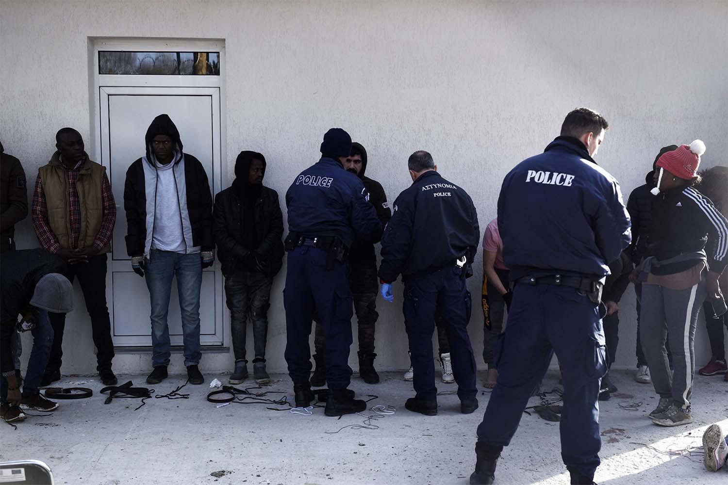 Greek policemen check detained migrants at a border police station in the village of Neo Cheimonio, Evros region