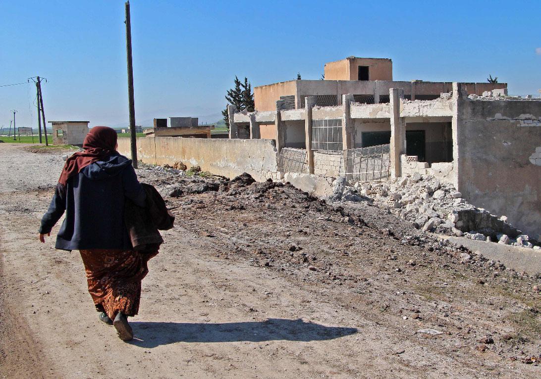 A displaced Syrian woman walks past a school that was reportedly targeted in a regime forces' air strike in Syria's northwestern Idlib province
