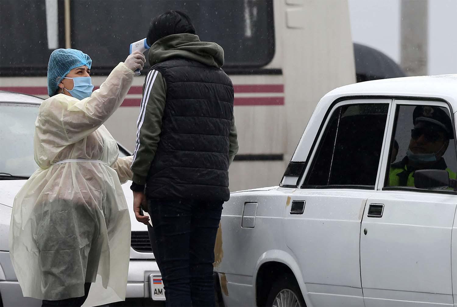 A medical worker in protective suit checks the body temperature of a person at a checkpoint in the city of Vagharshapat