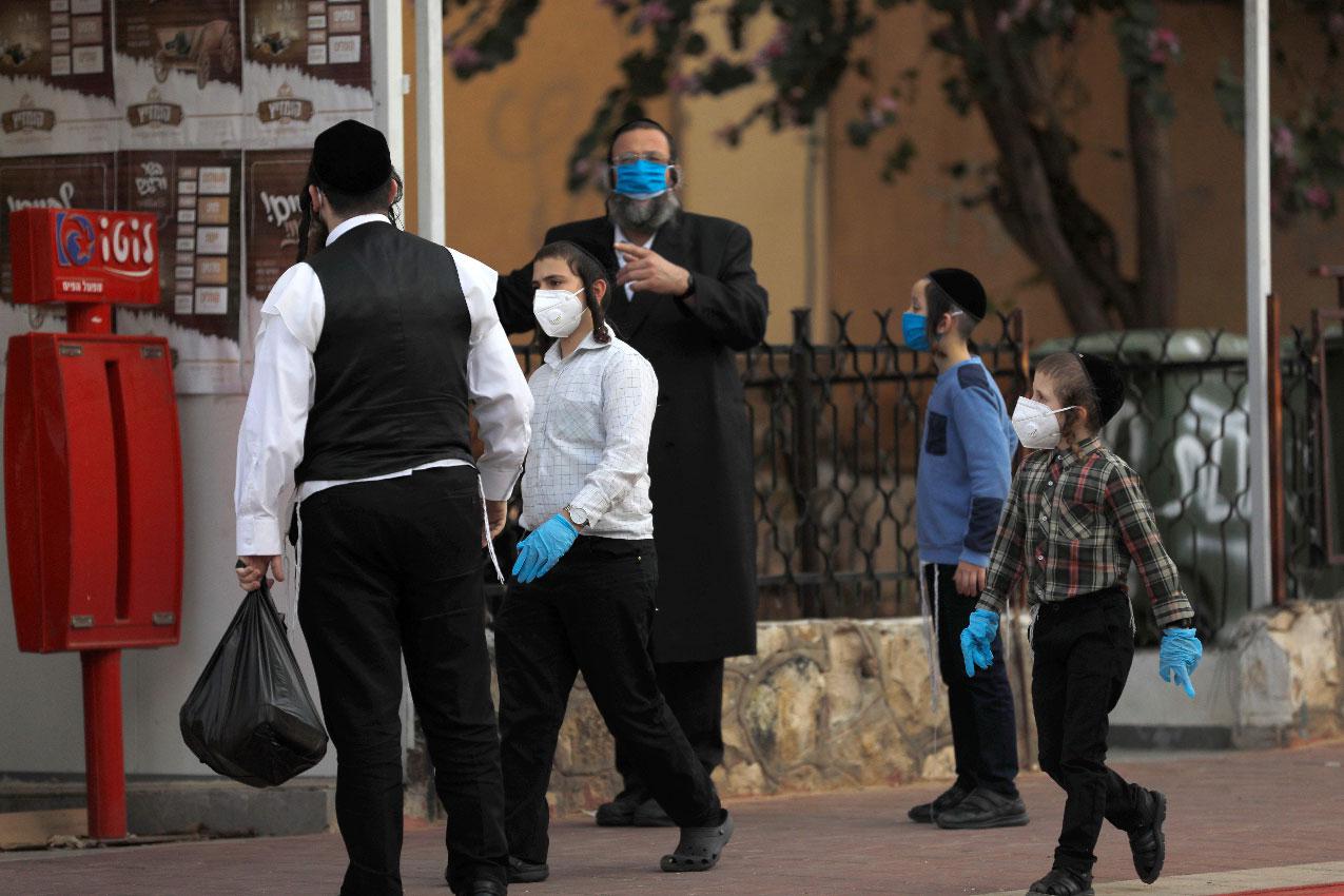 Ultra-Orthodox Jewish men and children wearing protective masks gather in a street