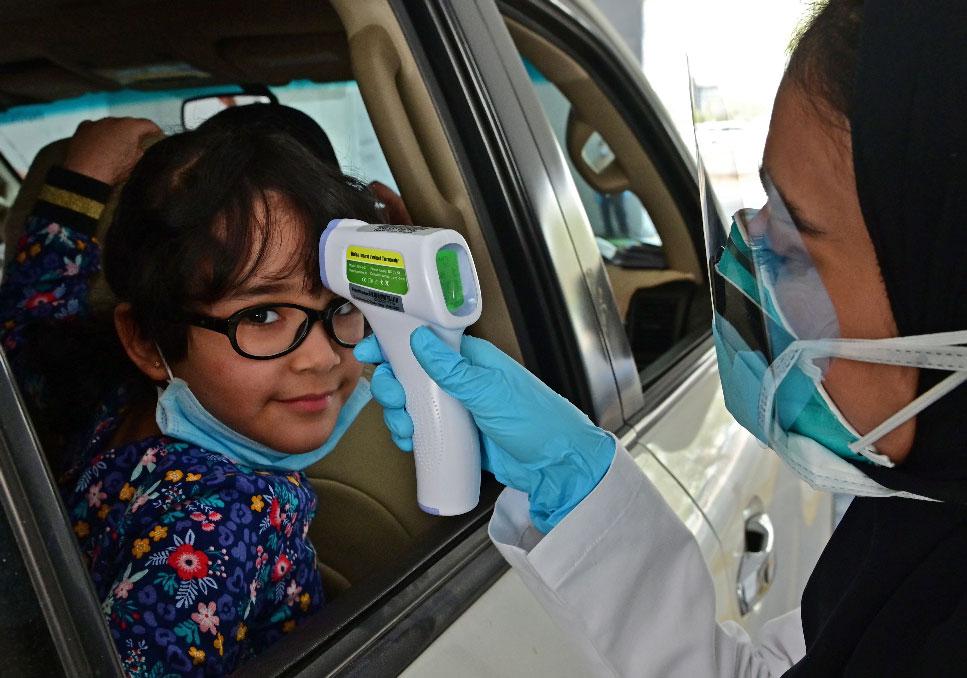 A nurse measures the body temperature of a young girl at a drive thru testing centre for COVID-19 in Abu Dhabi
