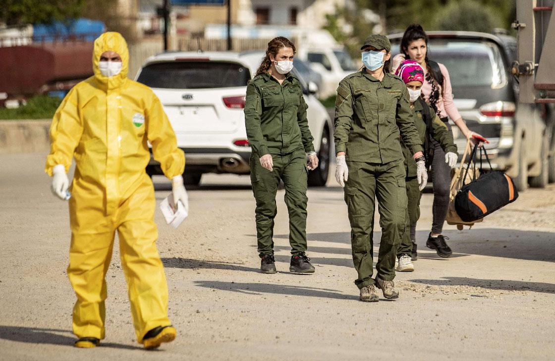 Members of Kurdish security and the Kurdish Red Crescent in protective gear escort a passenger upon arrival from Damascus