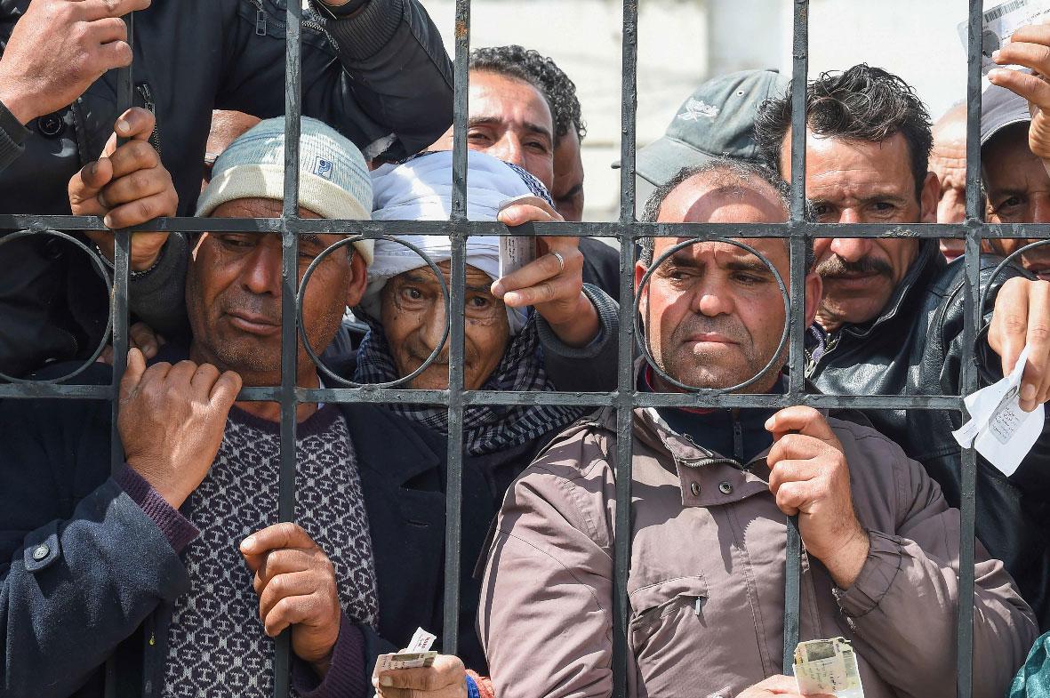 Impoverished Tunisian citizens gather with their ID cards to claim financial aid in Mnihla, Tunisia
