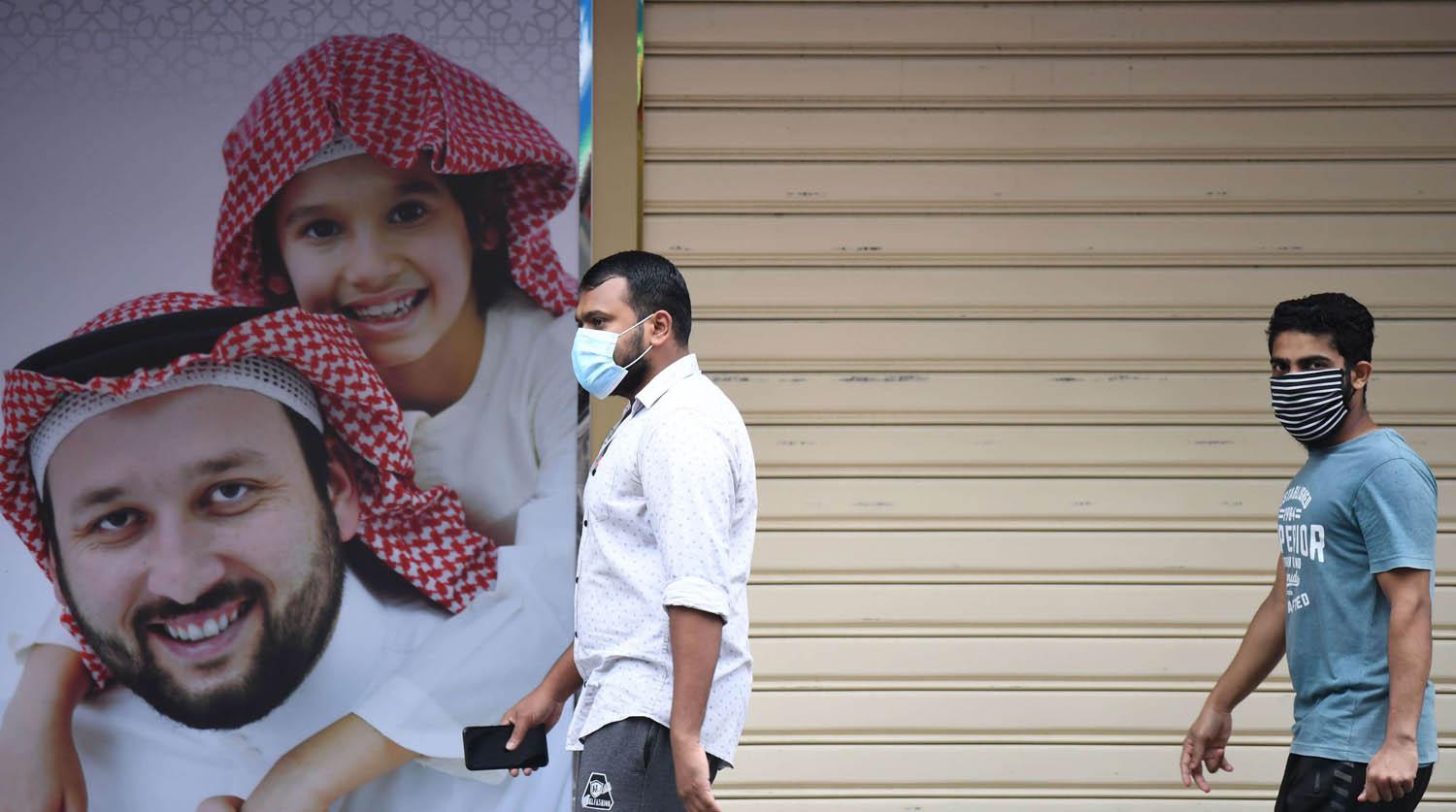 عمال اسيويون يمرون من أمام محال مغلقة في دبي