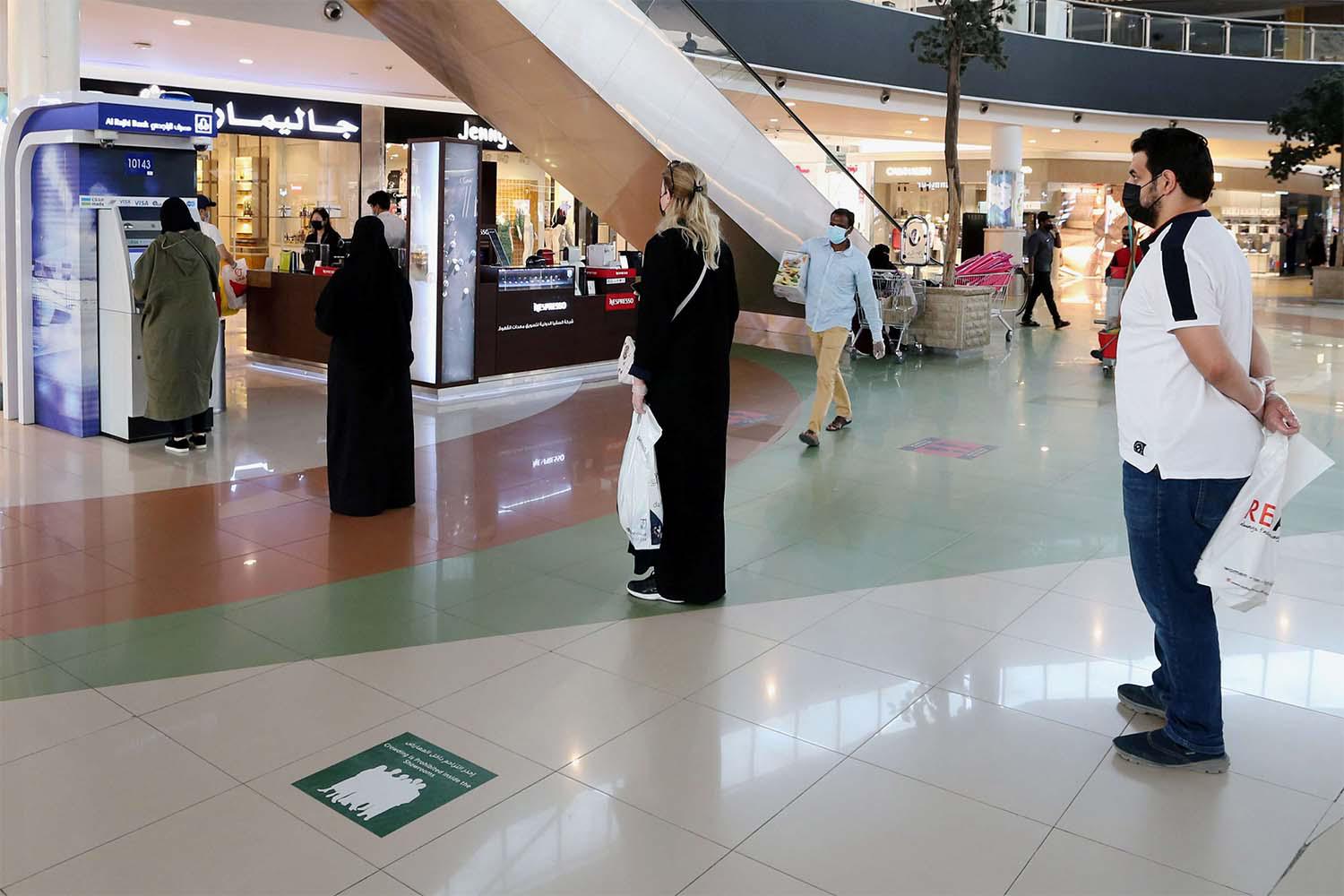 People line up while practicing social distancing to use an ATM at a shopping mall 
