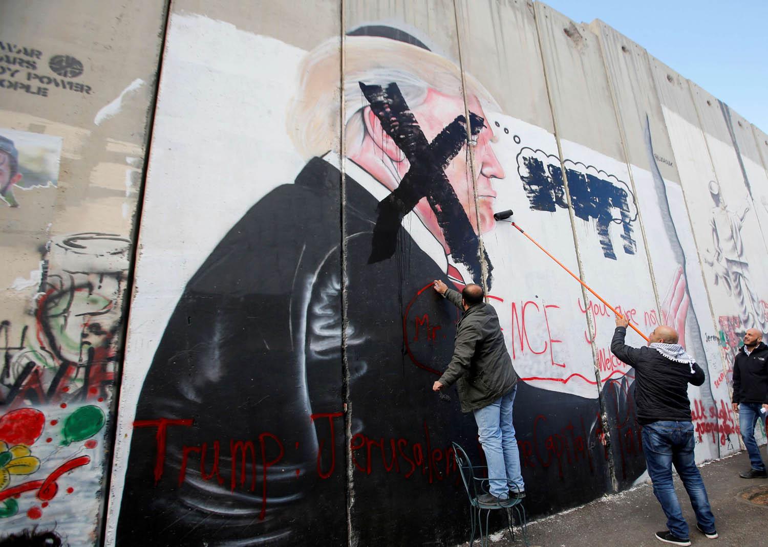 فلسطيني يشطب صورة جدارية للرئيس السابق دونالد ترامب من سور عازل بين إسرائيل والضفة الغربية