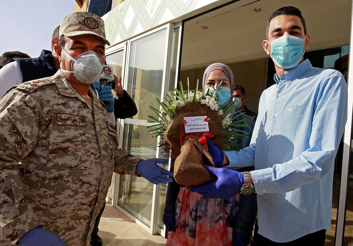 جندي أردني يحيي متزوجين حديثًا بالزهور أثناء مغادرتهما لمنتجع البحر الميت حيث تم عزلهما لمدة 14 يومًا