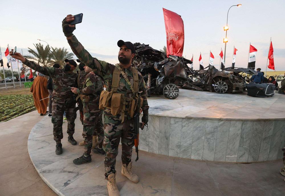 عناصر من الحشد يلتقطون صور سيلفي قرب موقع قتل فيه سليماني والمهندس حيث وضع هيكل محترق للسيارة التي كانت تقلّهما