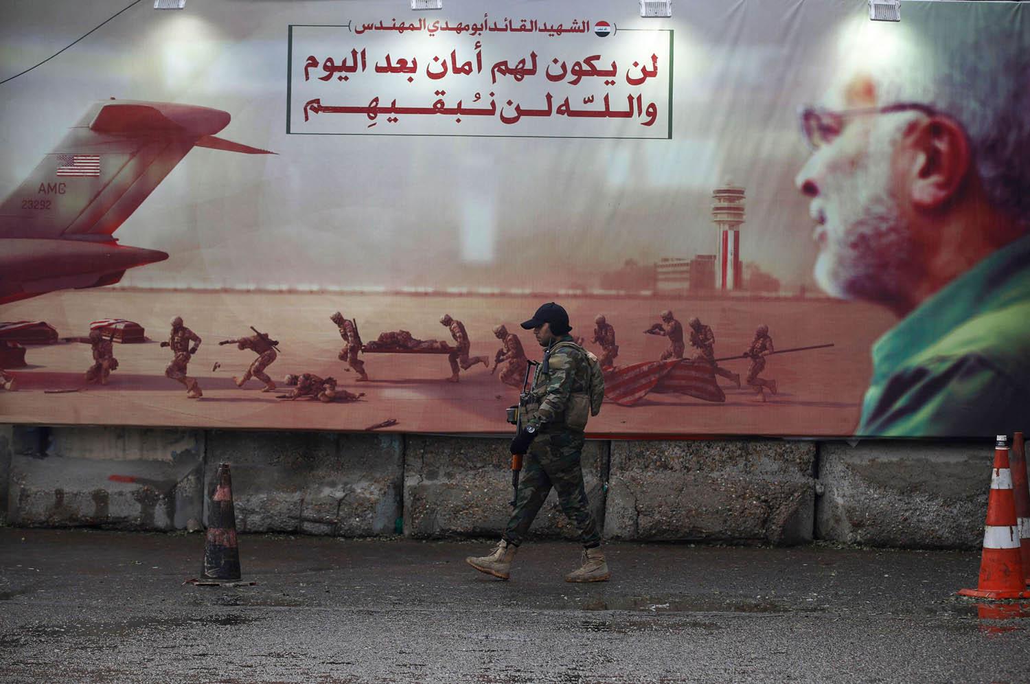 مقاتل من الحشد الشعبي أمام جدارية لأبو مهدي المهندس في بغداد