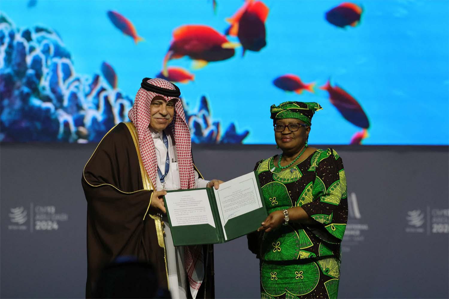 WTO Director-General of Ngozi Okonjo-Iweala and Saudi Minister of Commerce and Investment Majid al-Qasabi pose for a picture with signed documents during a session on Fisheries Subsidies