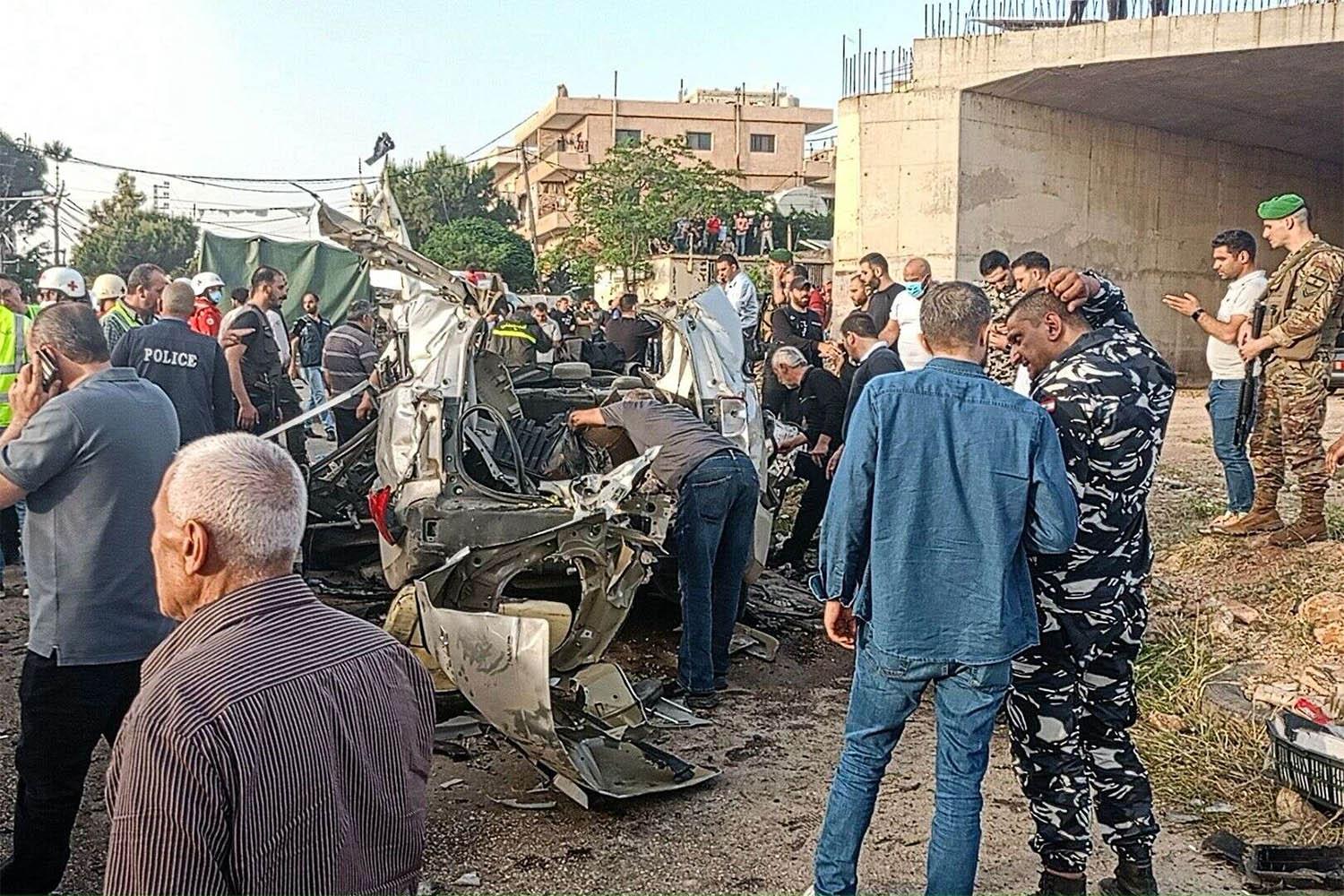 Lebanese army soldiers and onlookers gather around the carcasses of a car after it was hit by an Israeli strike