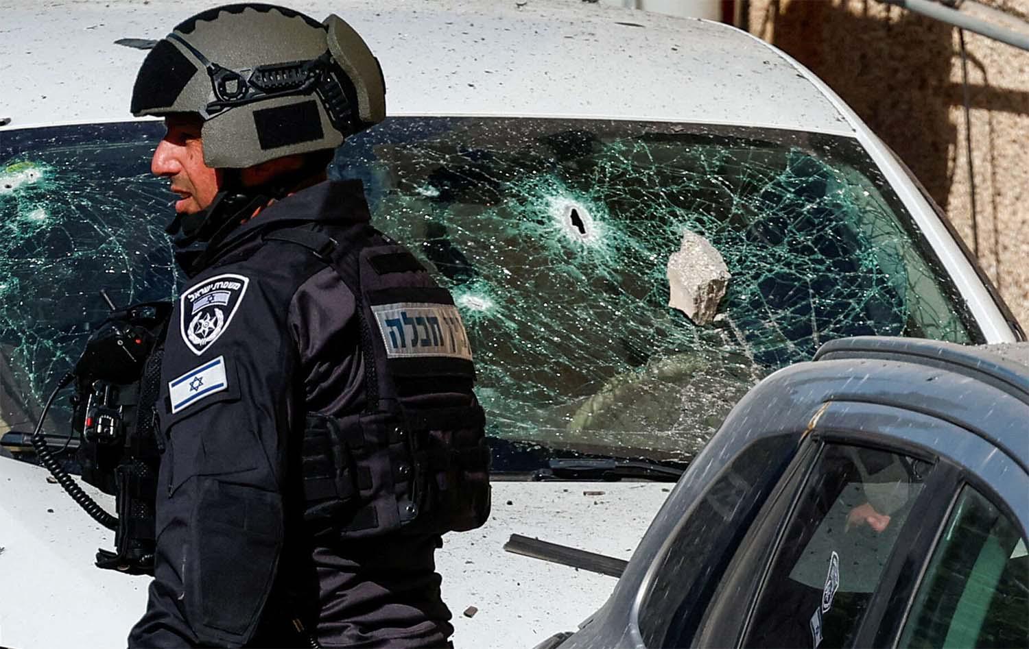An Israeli security forces member stands next to a damaged car at the site of a drone attack