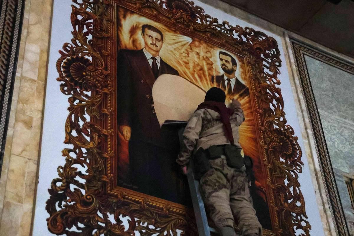 مقاتلو المعارضة يمزقون لوحة للرئيس بشار الأسد وأخيه الراحل باسل في مطار حلب